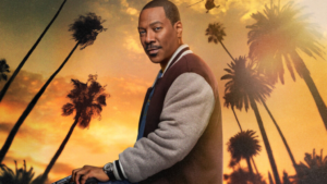 A person wearing a letterman jacket stands in front of a backdrop featuring palm trees against an orange sky at sunset.