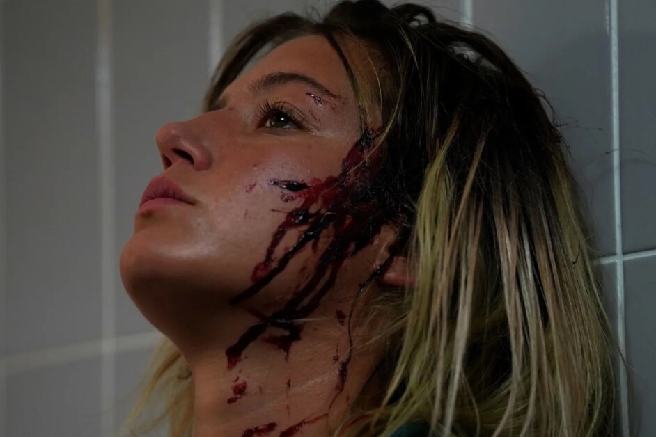 A person with blood on their face and neck is leaning against a tiled wall, looking upwards with a blank expression.