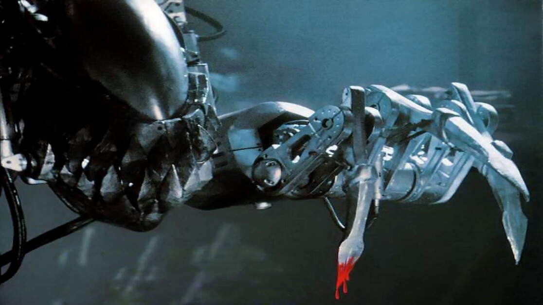 A robotic arm with sharp, claw-like fingers is shown holding a bloodied piece of human flesh against a dark background.