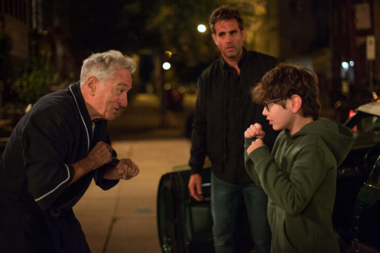 ‘Ezra’ Review – Good Intentions, Bad Decisions An older man teaches a young boy a boxing stance while a middle-aged man watches on a dimly lit street.