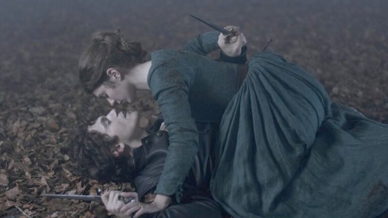 ‘My Lady Jane’ Review – A Gleeful, Steamy, And Delightful Alternative Take On History Two people in period costumes are on a leaf-covered ground, each holding daggers. The woman is on top of the man, who is lying down. Both appear engaged in a tense confrontation.