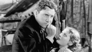 ‘Man’s Castle’ Blu-Ray Review – Loretta Young Is A Light In This Dour Pre-Code Drama A man with a serious expression rests his chin on his fist while a woman in a patterned dress looks up at him intently. The image is in black and white.
