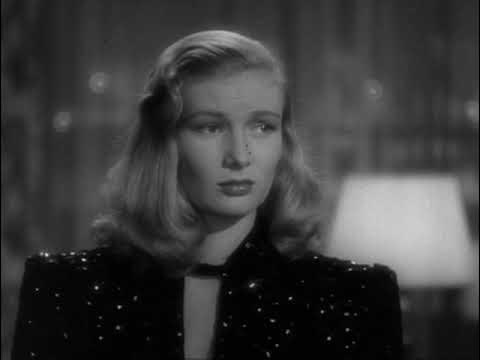 Black-and-white image of a woman with wavy blonde hair, wearing a dark, sparkly outfit. She has a serious expression and is facing slightly to the right. A lamp is visible in the blurred background.
