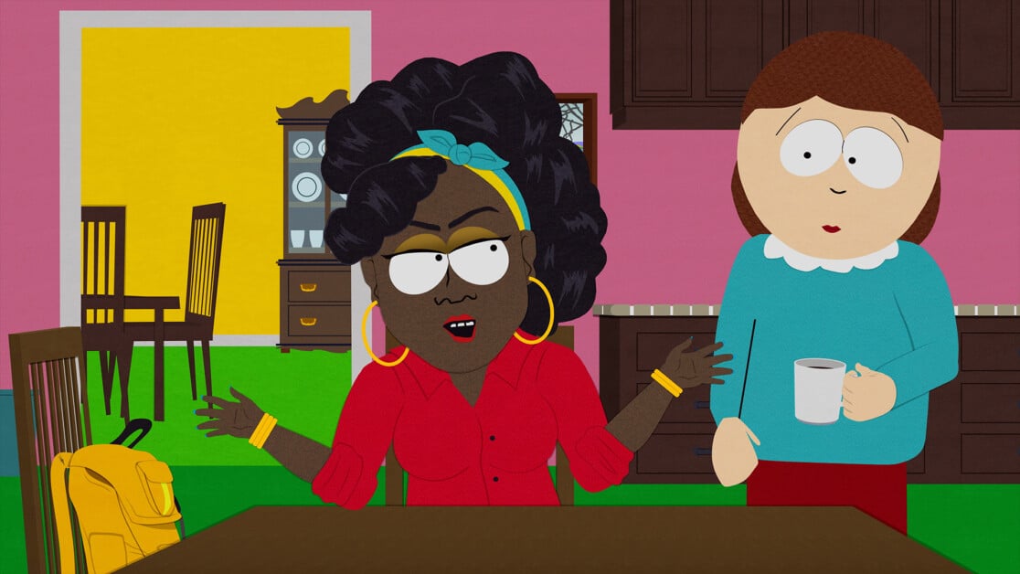 Two animated characters are in a kitchen. One has dark skin, curly hair, and is gesturing while speaking. The other has light skin, straight hair, and is holding a mug. A yellow backpack sits nearby.