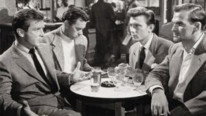 ‘The Good Die Young’ Blu-Ray Review – A Jumbled & Unsatisfying British Film Noir Four men in suits sit around a small round table with drinks in a busy bar, engaged in a serious conversation.