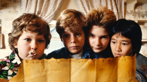 Four children, two with lighter hair, one with dark hair, and one with unkempt curly hair, closely examine an old, yellowed map.