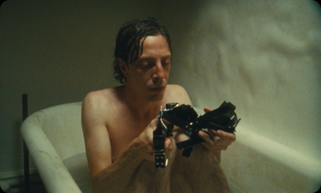 A person with wet hair sits in a bathtub, focusing intently on a mechanical device they're holding.