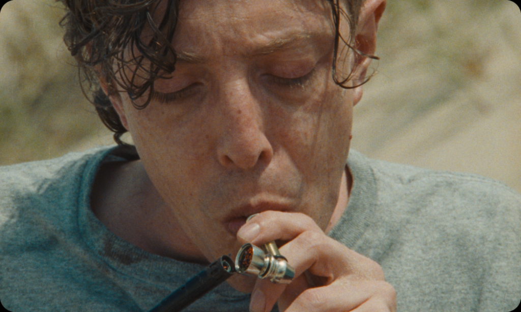 A person wearing a grey shirt is lighting a pipe, holding it close to their mouth with a concentrated expression.