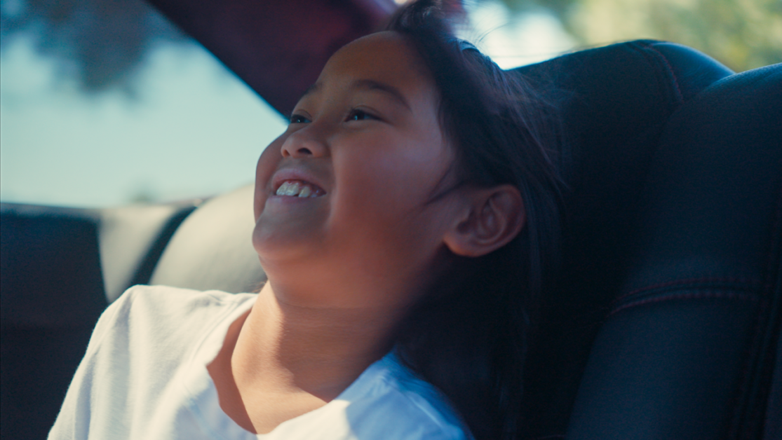 A smiling child sits in the back seat of a car.