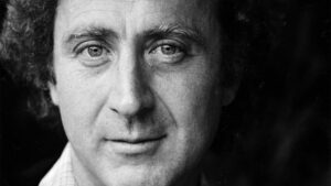 ‘Remembering Gene Wilder’ Blu-Ray Review – A Loving Portrait Of A Screen Icon A black-and-white close-up portrait of a man with curly hair, displaying a neutral expression and looking directly into the camera.