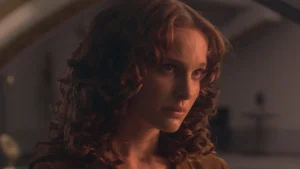 A person with curly hair looks intently off to the side in a dimly lit setting.