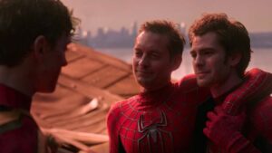 Three individuals dressed in Spider-Man suits, two standing close with one having his arm around the other's shoulder, while another faces them. The background features a city skyline during sunset.
