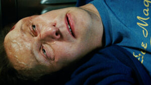 A close-up of a person lying down, wearing a blue shirt and blue jacket, with a concerned expression on their face.