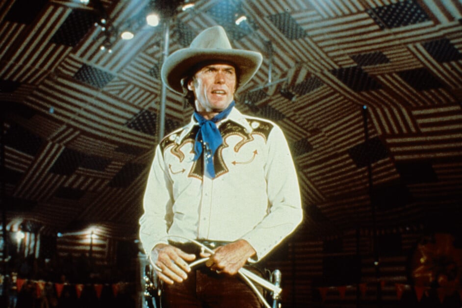 A man in a cowboy hat and Western attire performs on stage under a tent decorated with striped patterns.