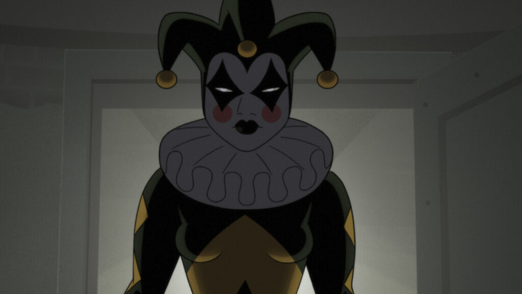A person dressed in a jester outfit with dark makeup stands in a dimly lit room.