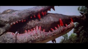 ‘Crocodile’ Blu-Ray Review – A Schlocky Giant Creature Feature Close-up of a large crocodile-like creature with red-tipped teeth biting another animal, set against a backdrop of trees and sky.
