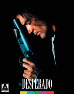 Man with long hair holds gun against his forehead, eyes closed, in a dark setting. The word "DESPERADO" is displayed at the bottom along with a logo.