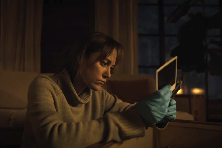 A person wearing blue gloves sits indoors, intently examining a photograph.