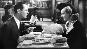 ‘Mr. & Mrs. Smith’ (1941) Blu-Ray Review – Carole Lombard Shines In Alfred Hitchcock’s Screwball Comedy A man and a woman are seated at a table in a restaurant, eating a meal with a loaf of bread and a white cat lying on the table between them.