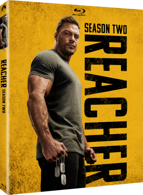 Blu-ray cover for "Reacher Season Two" showing a muscular man in a grey t-shirt holding dog tags, with a yellow background and bold text on the right side.