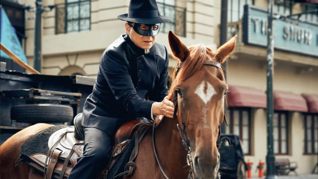 A person dressed in black and wearing a black mask rides a brown horse in an urban setting.