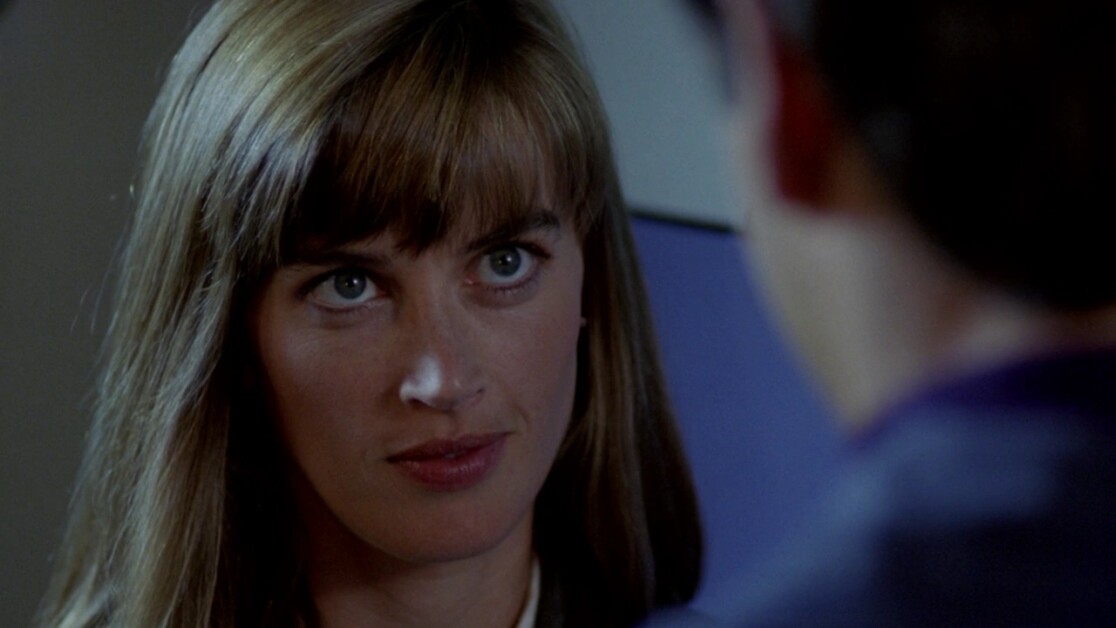 Close-up of a woman with long brown hair and bangs, looking intently at a person who is partially out of frame.