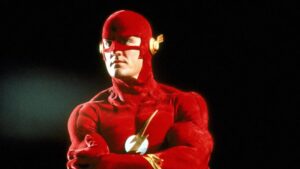 ‘The Flash’: The Complete Original Series Blu-Ray Review – ’90s Superhero Series Gets 5-Star Upgrade A person in a red superhero costume with a lightning bolt symbol on the chest and gold accents on the mask stands with arms crossed against a dark background.
