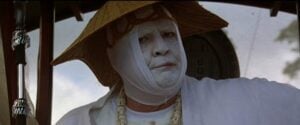 ‘The Island Of Dr. Moreau’ (1996) Collector’s Edition Blu-Ray Review – A Notorious Oddly Fascinating Misfire Person wearing white face paint, a conical hat, and traditional clothing, with a stern expression.