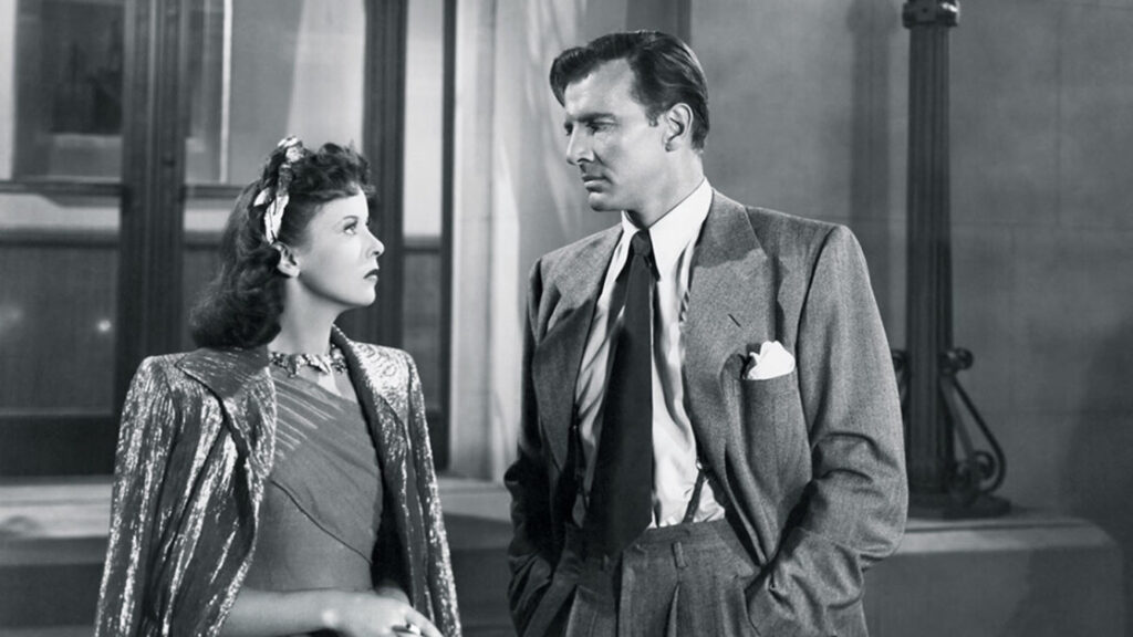 A man and a woman stand facing each other in formal attire. The image is in black and white and has a classic, vintage look.