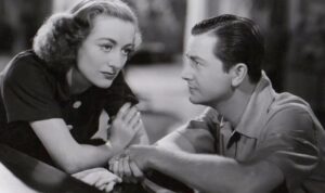A woman and a man are engaged in a serious conversation, with both leaning towards each other and clasping hands.