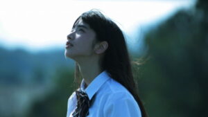A person in a white shirt with a tie looks upward against a blurred outdoor background.