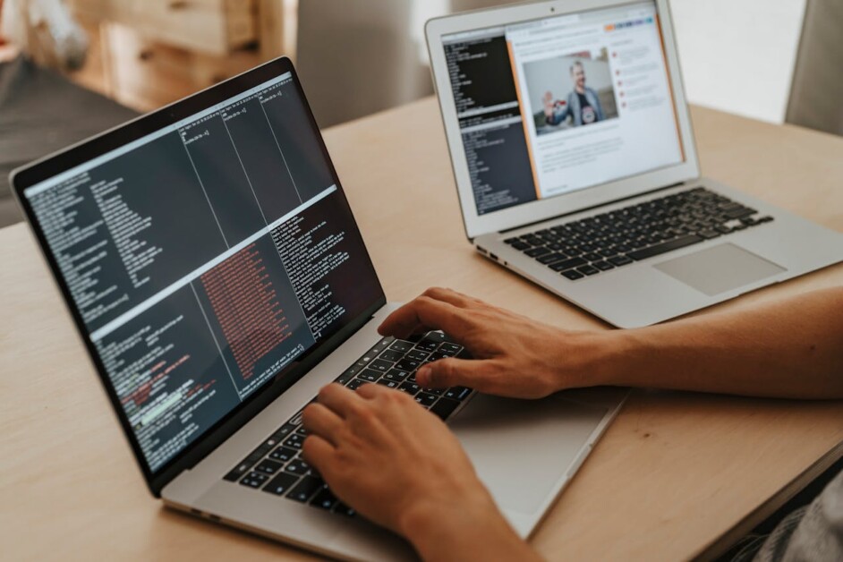 Person typing code on a laptop with another laptop displaying a web page in the background.