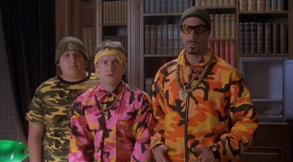 Three people stand in front of bookshelves, wearing brightly colored camouflage outfits and accessories.