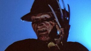A menacing figure with a burned face and a gloved hand wielding sharp blades stands in a dark, eerie setting.