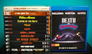 A stack of 11 DVD cases and a Blu-ray case. The titles visible include "Tokijiro: Lone Yakuza," "A Man Called Tiger," "Death to Smoochy," and others. The cases are arranged upright against a teal background.