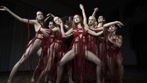 Imprint Films Announces Summer Titles Including Works From Robert De Niro, Mario Bava, Tobe Hooper & More A group of dancers in red costumes striking dramatic poses with expressive arm movements on a dimly lit stage.