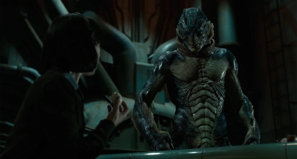 A person holds a small object while facing a tall humanoid creature with amphibian features in a dimly lit industrial setting.