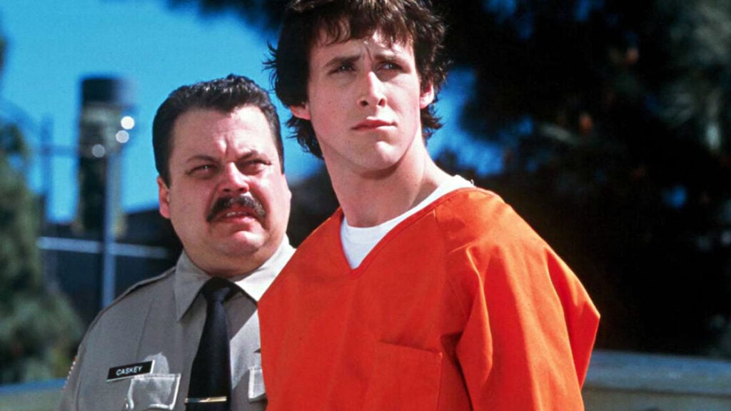 A person in an orange jumpsuit stands beside a uniformed officer outdoors.