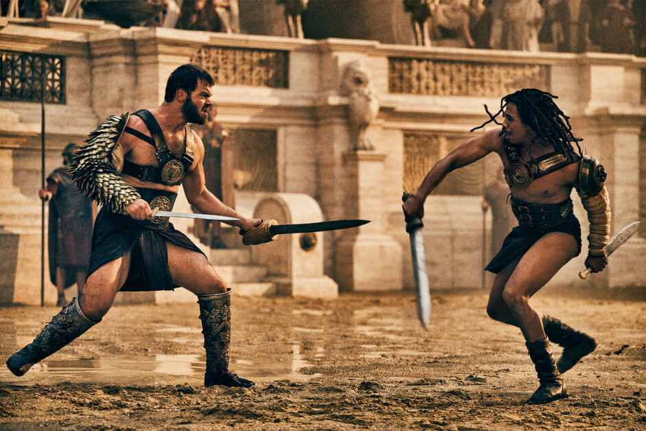 Two armored gladiators face off with swords in an ancient Roman arena, surrounded by a cheering audience.
