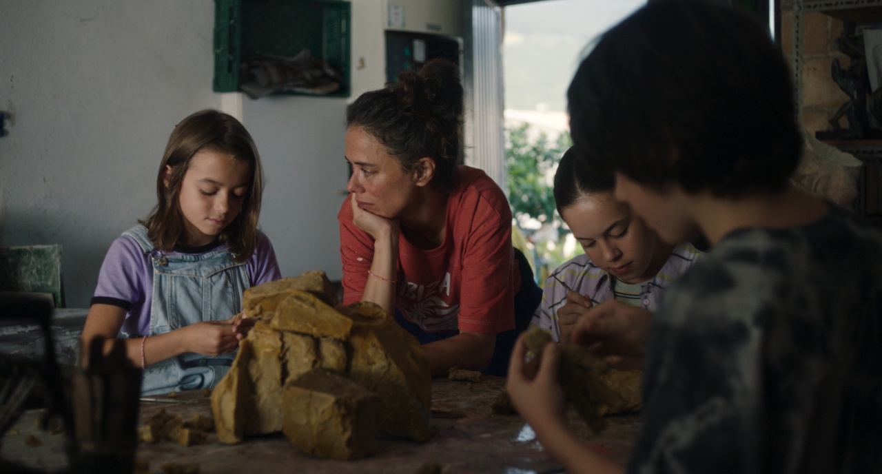 Four people gathered around a table, sculpting with clay. They are focused, and the setting is indoors with natural light filtering in.