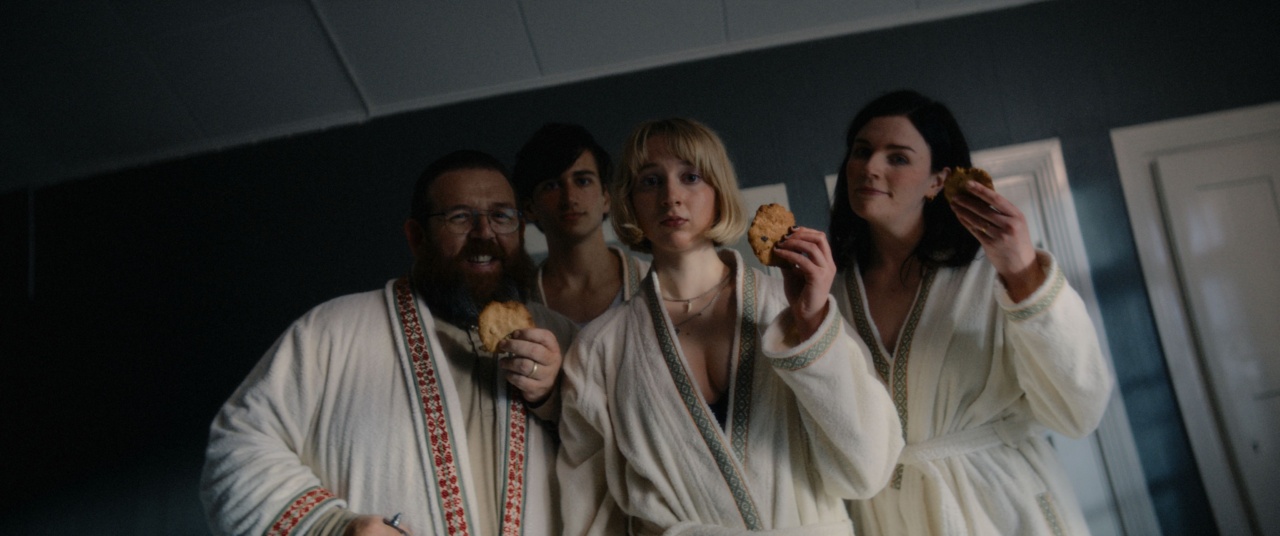 Four people in robes hold cookies and look at the camera in a dimly lit room.