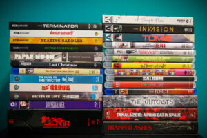 A stack of DVD and Blu-ray movie cases, featuring titles like "The Terminator," "Blazing Saddles," and "Susperia," against a teal background.