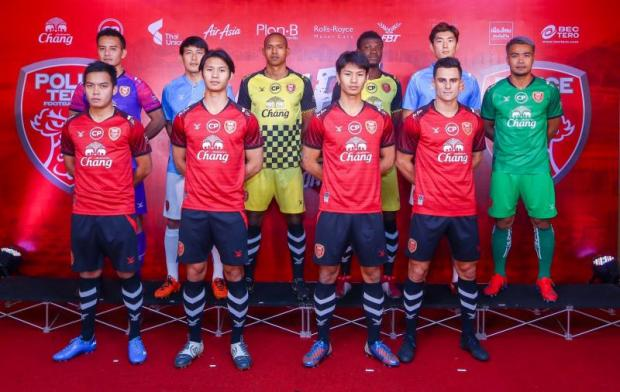 A soccer team in red and black uniforms poses for a group photo on a red carpeted area with a branded backdrop.
