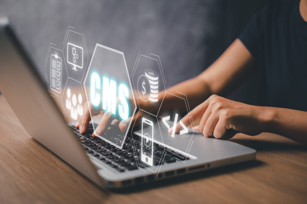Person typing on a laptop with virtual icons floating above, including CMS, cloud storage, and coding symbols.