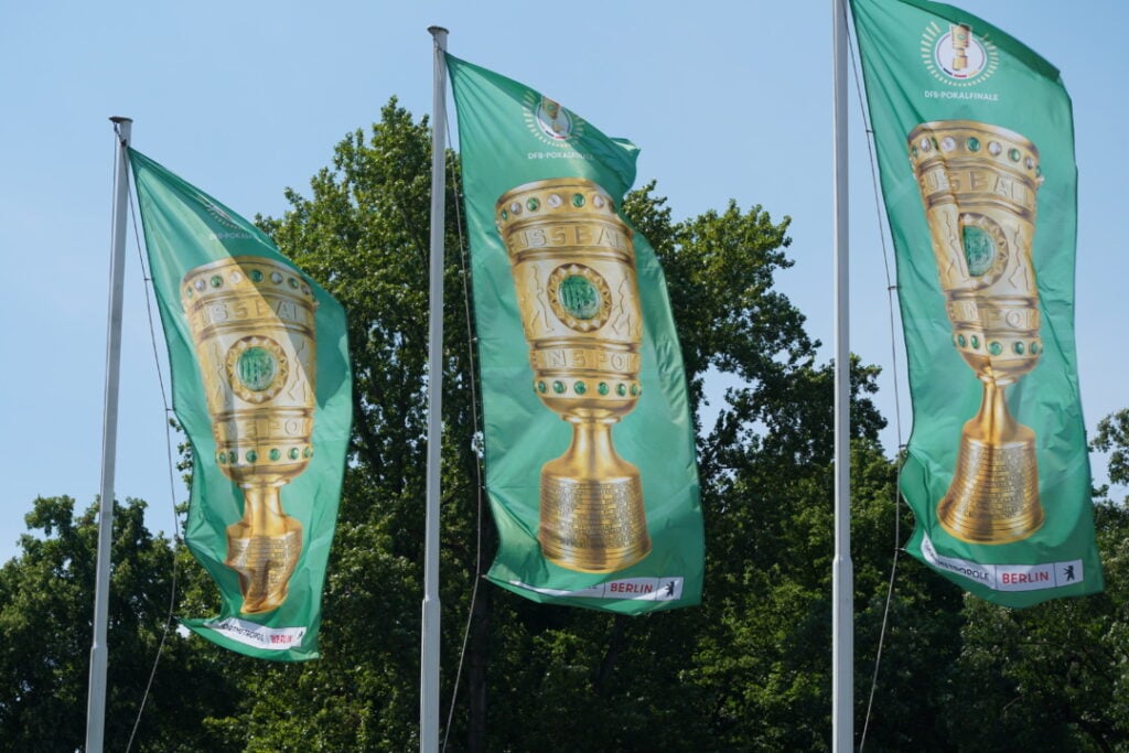 Three green flags display images of a gold trophy with the text "DFB Pokal Finale" against a backdrop of green trees.