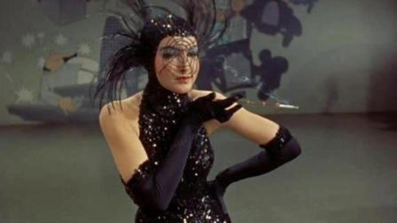A person in a black sequined outfit with long gloves and a feathered hat stands with an outstretched arm, holding a cigarette holder. The background is an abstract painting.