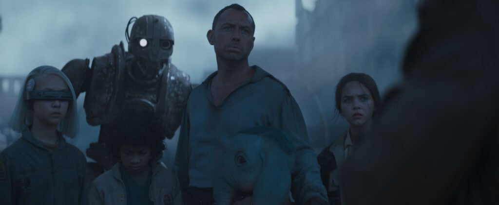 A group of people and a robot stand in a misty environment, looking intently in the same direction.