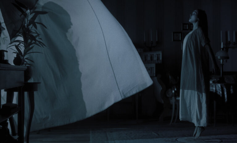 A woman in a white gown levitates in a dimly lit room, with a large billowing sheet nearby.