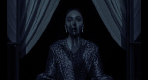A person stands in front of a window with drawn curtains, wearing patterned clothing, in low-light conditions.