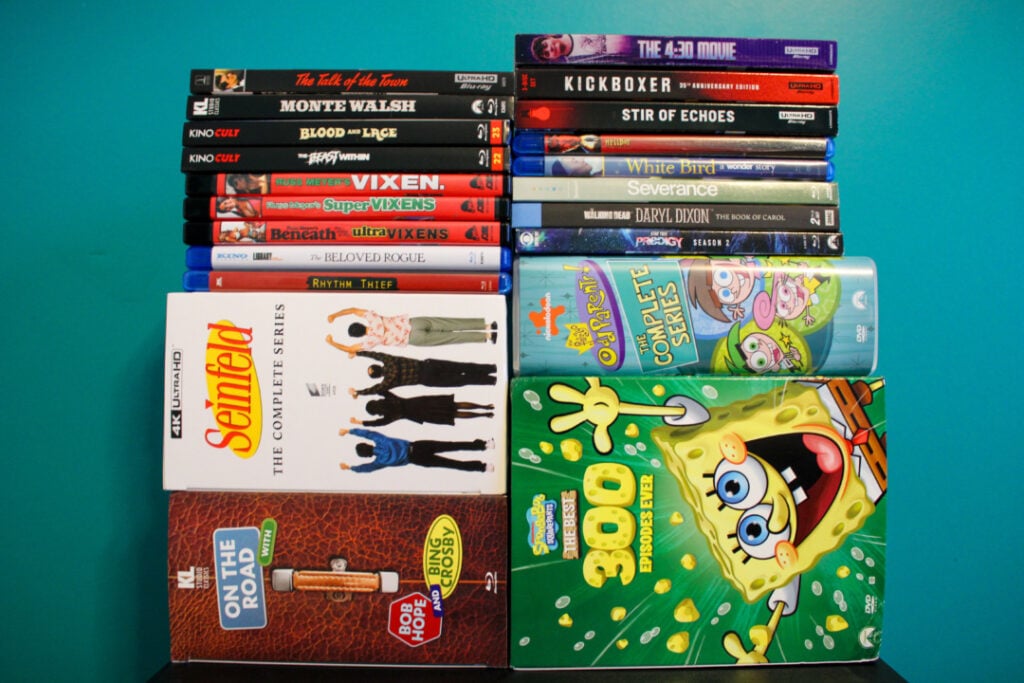 A collection of DVDs and Blu-rays, including titles like "Seinfeld," "SpongeBob SquarePants," and various movies, arranged neatly against a blue background.